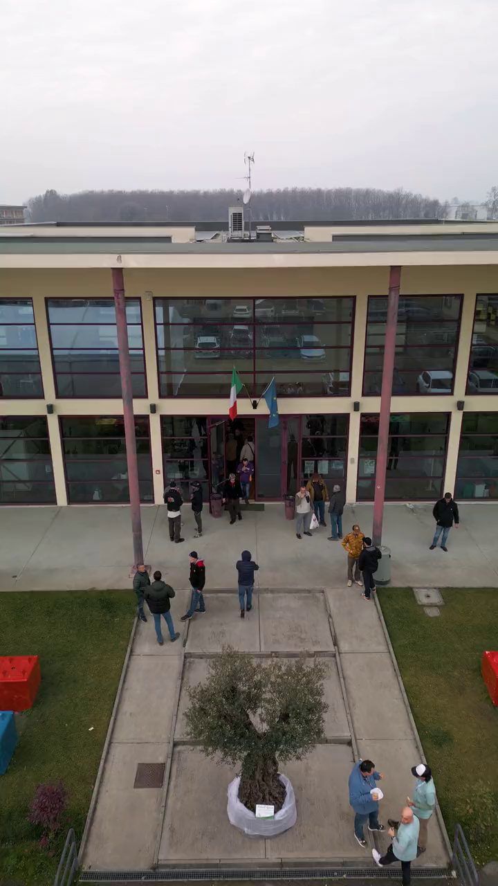 Visitatori davanti alle vetrate d'ingresso, con il tendone bianco sul piazzale