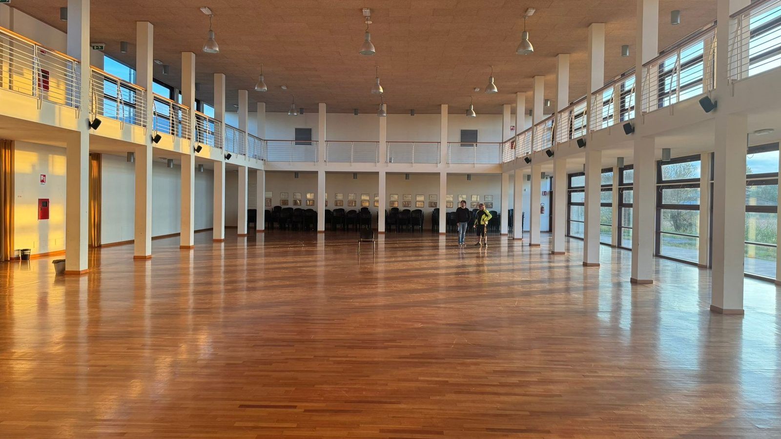 La sala polivalente vuota: parquet, colonne bianche e il ballatoio lungo le pareti